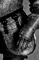 Black and white close-up photograph of ornate armor showing an articulated steel gauntlet, forearm and overlapping protection around the hip.