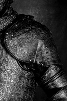 Black and white close-up photograph of a suit of armor showing overlapping steel plates across the shoulder, upper arm and chest.