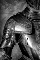 Black and white close-up photograph of historic armor showing a decorated shoulder, upper arm and breastplate.