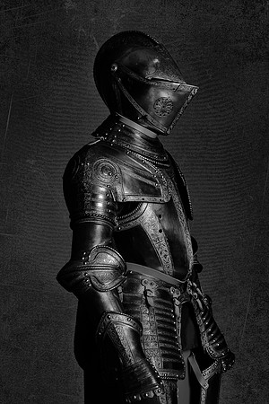 Black and white profile photograph of a historic suit of armor standing upright against a dark textured background.