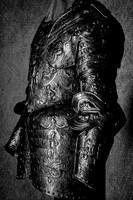 Black and white photograph of an ornate full suit of armor viewed from the side, showing its decorated breastplate, arm and overlapping leg protection.